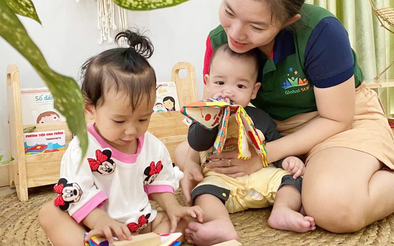 Cô ngồi trên thảm chơi đồ chơi vải cùng hai bé nhỏ